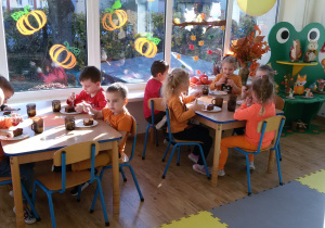 Widok na siedzące przy dwóch stolikach dzieci, które jedzą ciasto dyniowe.