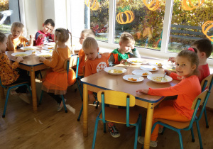 Widok na siedzące przy dwóch stolikach dzieci, które jedzą zupę dyniową.