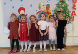 Widok na grupę dziewczynek pozujących do zdjęcia na tle bożonarodzeniowej dekoracji.