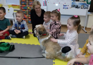 Widok na siedzące na dywanie dzieci. Marysia głaszcze pieska.