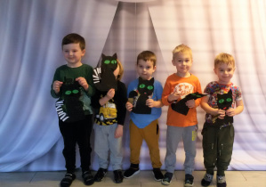 Pięciu chłopców pozuje do zdjęcia z papierowymi czarnymi kotami.