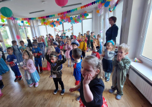Dzieci poprzebierane w stroje karnawałowe tańczą na balu.