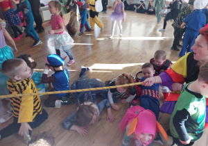 Dzieci czołgają się po podłodze przechodząc pod sznurkiem w trakcie zabawy karnawałowej.