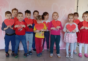 Dzieci pozują do zdjęcia trzymając przed sobą serca z papieru.