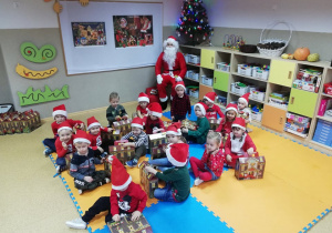 Grupa dzieci w czerwonych strojach pozuje do zdjęcia ze Świętym Mikołajem.