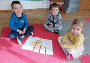 Widok na troje siedzących dzieci, które prezentują ułożonego przez siebie dinozaura.