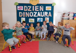 Dzieci naśladujące dinozaura pozują do zdjęcia grupowego.