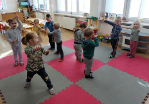 Widok na dzieci naśladujące w tańcu ruchy dinozaura.