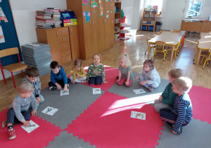 Dzieci siedzące w kółeczku oglądają zdjęcia przedstawiające różne dinozaury.