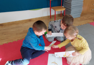 Troje dzieci układa z puzzli obrazek dinozaura.