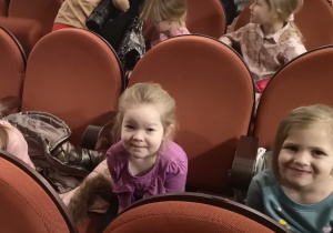 Widok na dwie dziewczynki siedzące na widowni w ŁDK. W tle widać dzieci zajmujące miejsca na widowni.