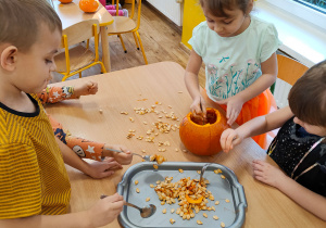 Dzieci przy stoliku wydrążają miąższ z dyni przy użyciu łyżki.