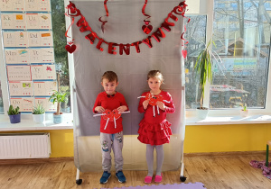 2 dzieci pozuje do zdjęcia stojąc i trzymając w ręku serca.
