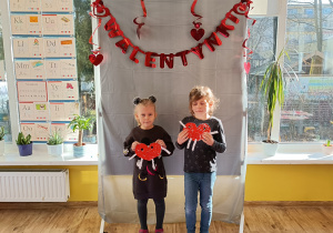 2 dzieci pozuje do zdjęcia stojąc i trzymając w ręku serca.