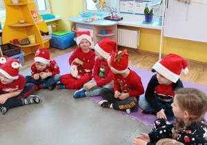 Dzieci siedzą na macie i przekazują sobie „skarpetę Mikołaja”, z której wyciągają słodki upominek.