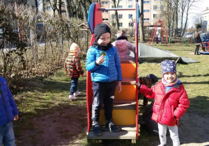 Widok na dziewczynkę i stojącego na stopniach zjeżdżali chłopca, który trzyma w ręku zielony listek. W tle widać bawiące się dzieci.