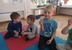 Widok na siedzące na macie dzieci, które trzymają w rękach woskowe świeczki.