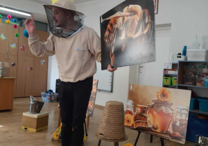 Widok na pszczelarza podczas prezentacji obrazów związanych z życiem pszczół.