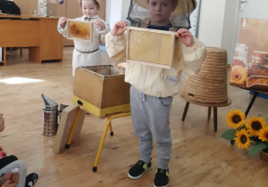 Dziewczynka i chłopiec prezentują akcesoria pracy pszczelarza.