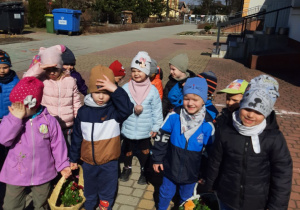 Dzieci stojące przed przedszkolem z koszykami, w których są kwiaty.