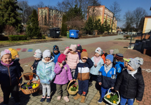 Zdjęcie grupowe dzieci stojących przed przedszkolem z koszami pełnymi kwiatów.