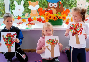Dzieci pozują do zdjęcia i prezentują wykonane przez siebie prace plastyczne.