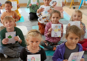 Widok na siedzące dzieci, które prezentują swoje stworki z liści.