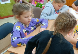 Widok na siedzące przy stoliku dzieci, które kolorują kolorowankę.
