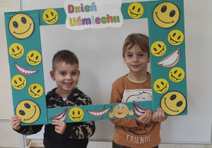 Chłopcy pozują do zdjęcia stojąc za ramką ozdobioną uśmiechami.