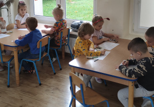 Widok na siedzące przy stolikach dzieci, które wykonują zadanie matematyczne.