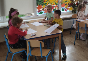 Widok na siedzące przy stoliku dzieci, które wykonują zadanie matematyczne.