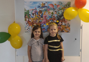 Dwie dziewczynki w bajkowych strojach pozują do zdjęcia na tle dekoracji z okazji Dnia Postaci z Bajek.