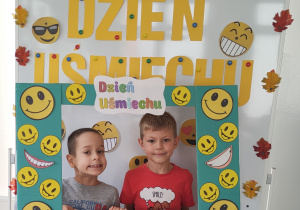 Chłopcy pozują do zdjęcia stojąc za ramką ozdobioną uśmiechami.