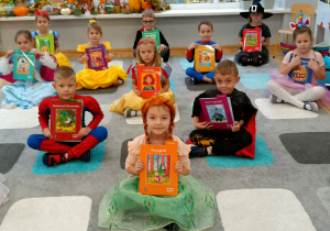 Widok na dzieci siedzące na dywanie, trzymające w dłoniach książki.