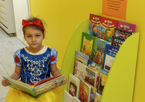 Widok na dziewczynkę siedzącą na krześle z otwartą książką przy biblioteczce przedszkolnej.