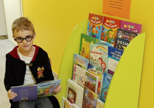 Widok na chłopca siedzącego na krześle z otwartą książką przy biblioteczce przedszkolnej.