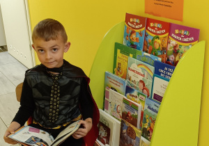 Widok na chłopca siedzącego na krześle z otwartą książką przy biblioteczce przedszkolnej.