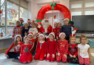 Dzieci w czerwonych strojach pozują do zdjęcia grupowego ze Świętym Mikołajem.