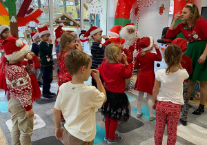 Widok na dzieci, które stoją przed św. Mikołajem i dotykają swój nos.