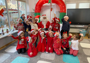Dzieci w czerwonych strojach pozują do zdjęcia grupowego ze Świętym Mikołajem.