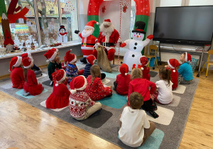 Widok na dzieci, które siedzą na dywanie przed św. Mikołajem.