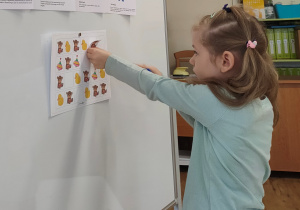 Dziewczynka wykonuje zadanie przy tablicy magnetycznej, przyczepia odpowiednio obrazki według konkretnego rytmu.