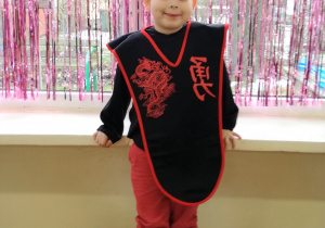 Chłopiec w kostiumie ninja pozuje do zdjęcia. W tle kurtyna dekoracyjna w kolorze różowym.