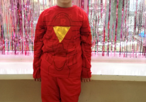 Chłopiec w stroju Avengers-a pozuje do zdjęcia. W tle kurtyna dekoracyjna w kolorze różowym.