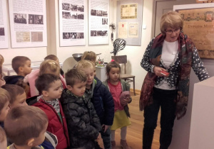 Dzieci słuchają jak pracownik muzeum opowiada o eksponatach.