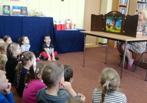 Widok na siedzące dzieci, które z uwagą oglądają legendę o Lechu, Czechu i Rusie prezentowaną w formie teatrzyku kamishibai przez Panią z biblioteki.