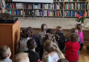 Widok na siedzące dzieci przed ekranem projektora, na którym ukazywane są pytania o Polsce.