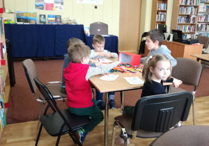 Widok na siedzące przy stoliku dzieci, które kolorują kartę pracy.