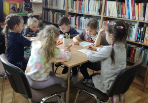 Widok na siedzące przy stoliku dzieci, które kolorują kartę pracy.