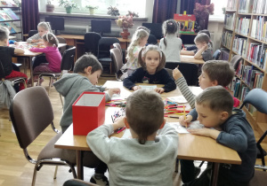 Widok na siedzące przy stolikach dzieci, które kolorują kartę pracy.